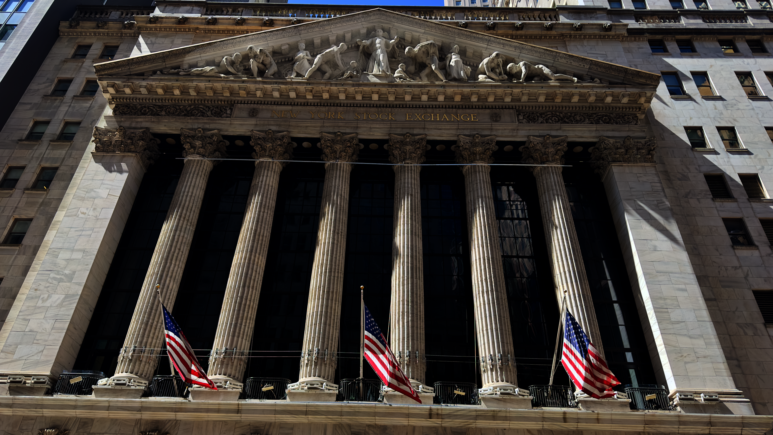 New York Stock Exchange building on Wall Street with American flags displayed, WNews stock photo taken April 2023.